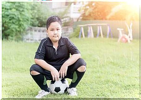 A child sitting on a ball in soccer gear. 